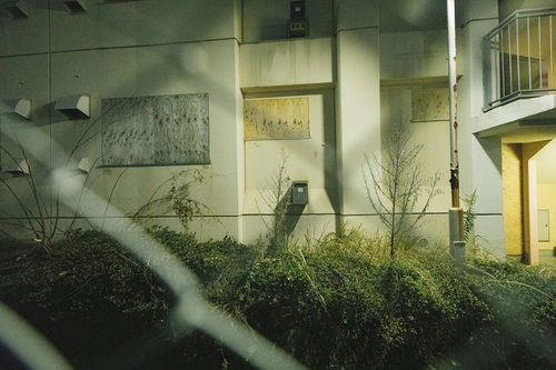 誰も住んでいない深夜の団地を金網越しに望む
