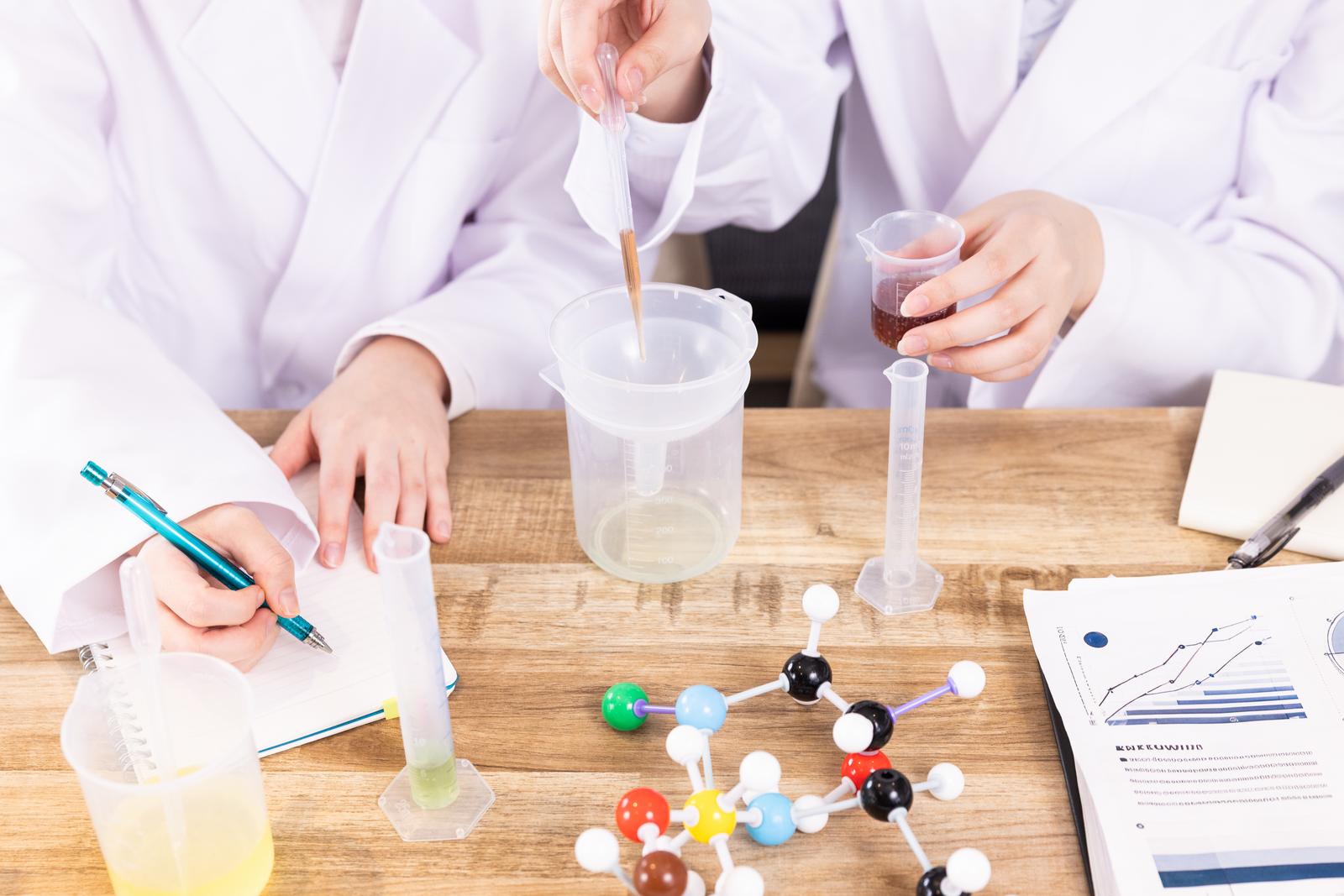 白衣の研究者が分子模型を手に持ち実験器具の前で作業する様子