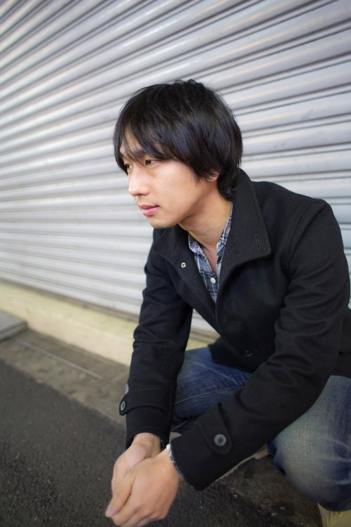 閉まったシャッターの前で座り込んでうなだれる男性