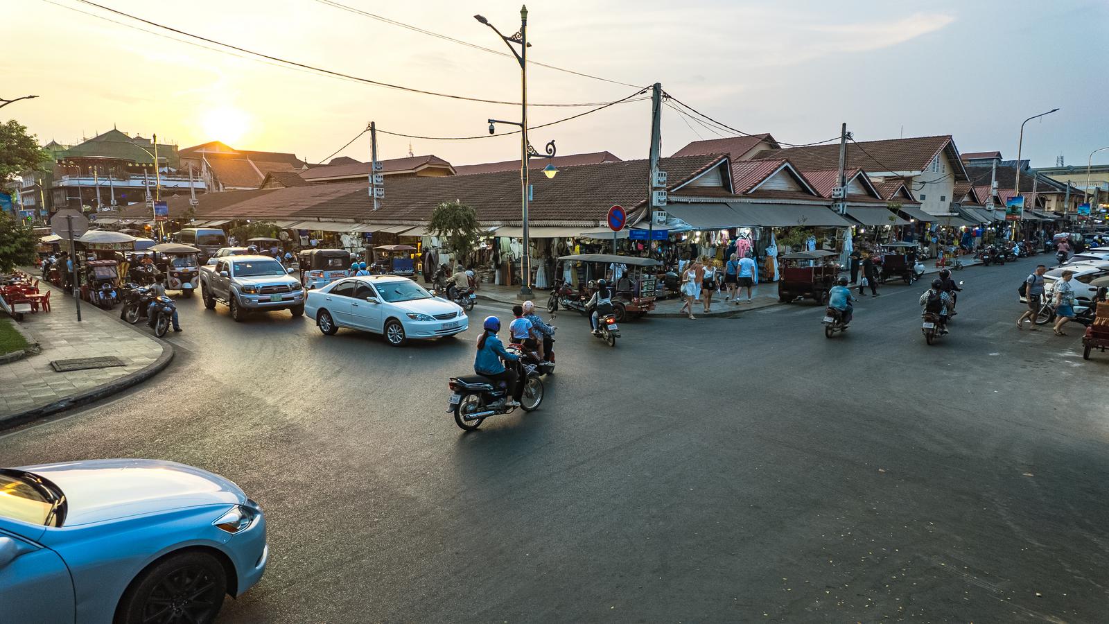 A dusk scene of blue taxis and motorcycles crossing an intersection in Siem Reap, Cambodia