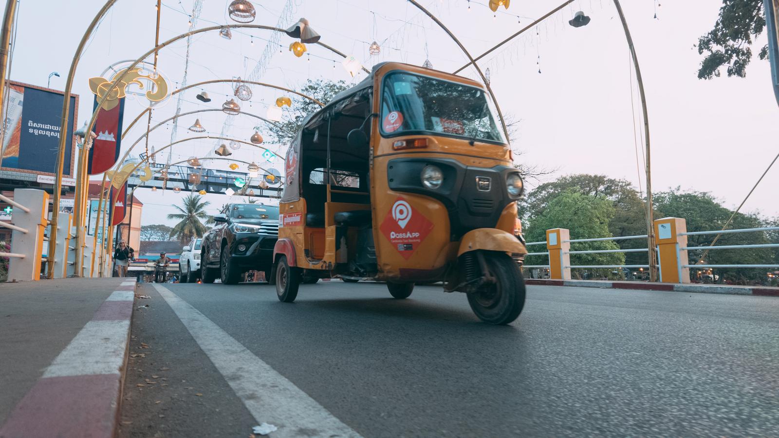 An orange tuk-tuk crossing a bridge in a cityscape