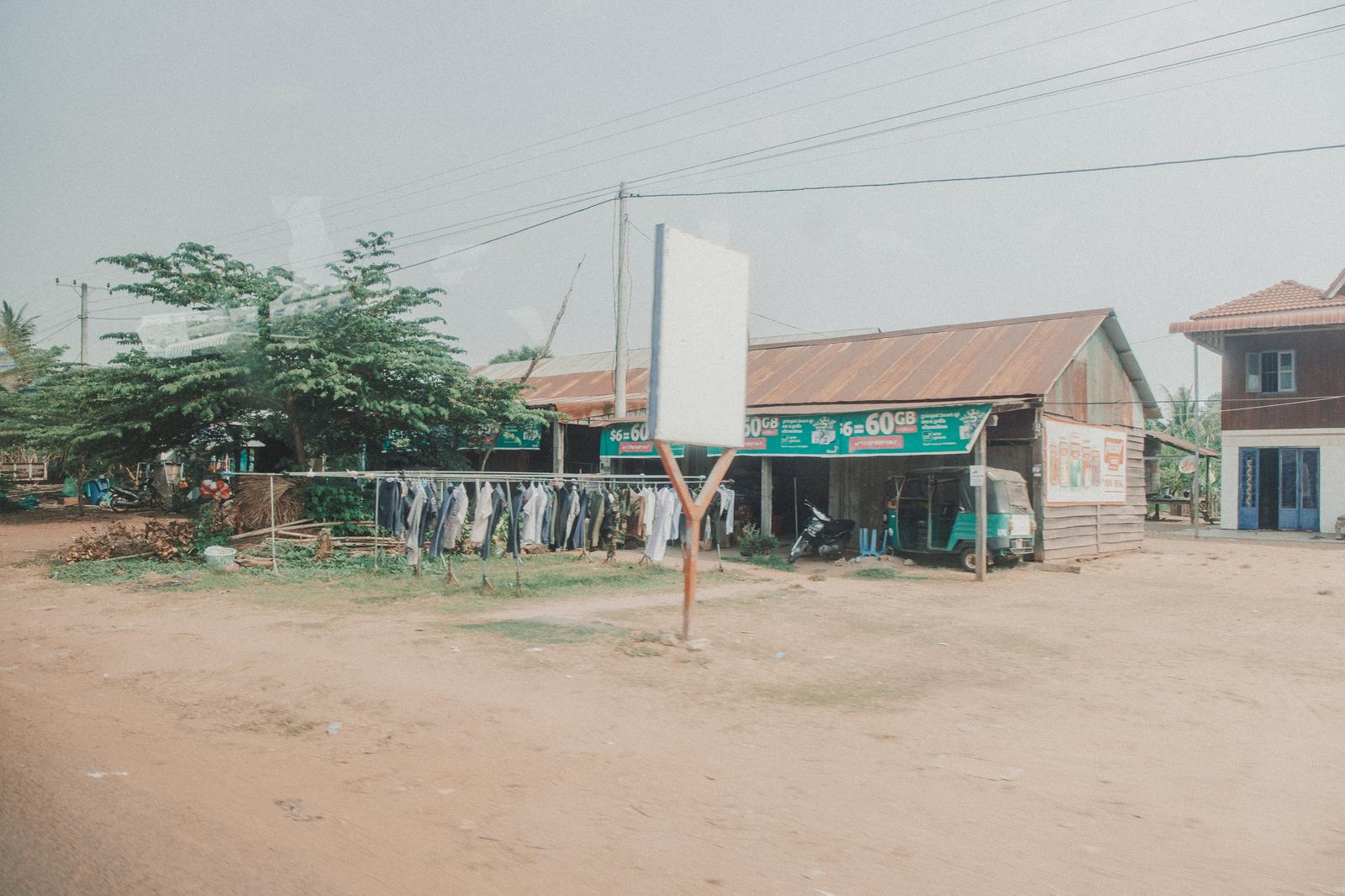カンボジアの田舎町で撮影した洗濯物が干された木造建物と未舗装道路がある東南アジアの地方都市街並み写真