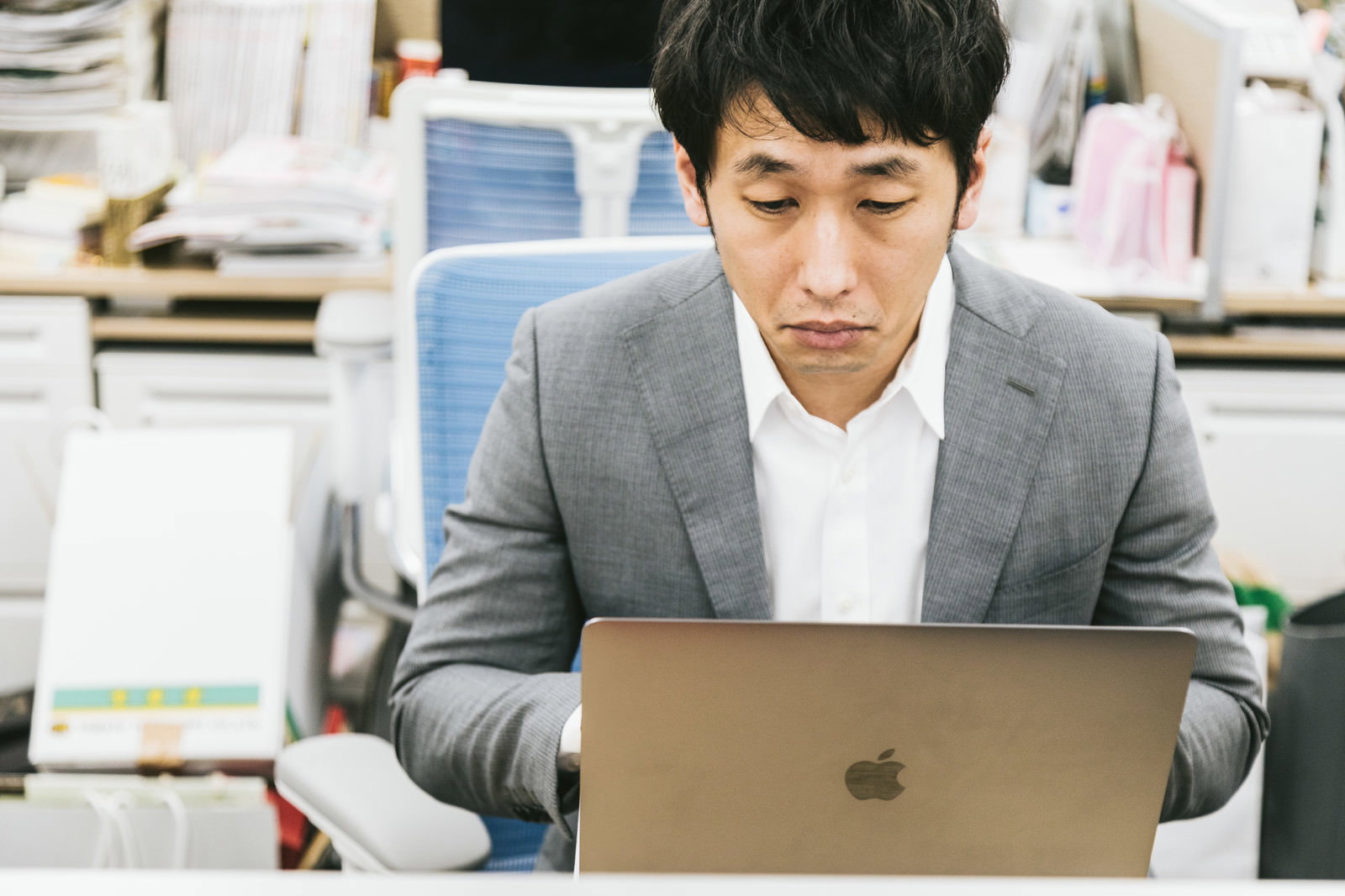 オフィスでノートパソコンの前で困惑した表情を見せるグレーのスーツ姿の男性［モデル：大川竜弥］