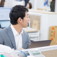 オフィスで隣席の部下に話しかけるチームリーダーの写真