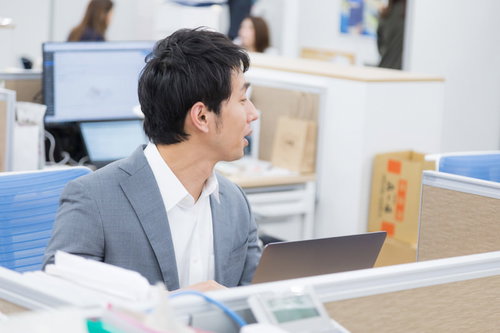 オフィスで隣席の部下に話しかけるチームリーダー