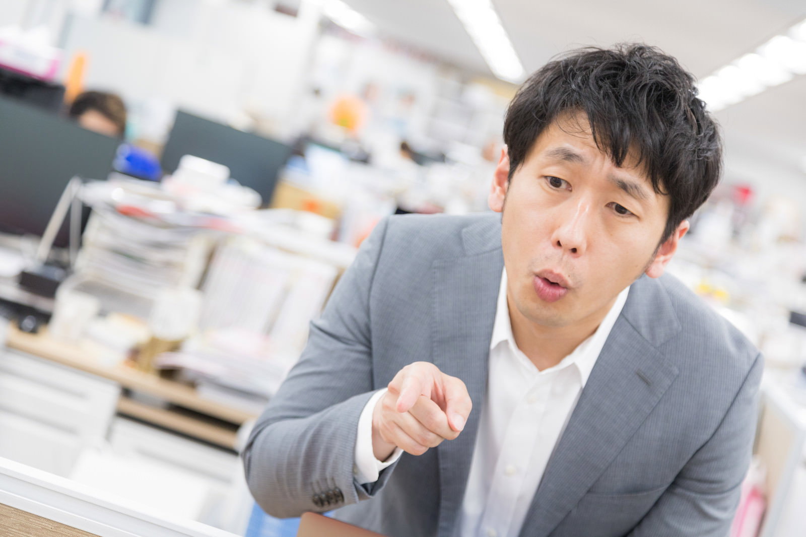 オフィスで右手の人差し指を指して説教する、グレーのスーツを着た男性［モデル：大川竜弥］