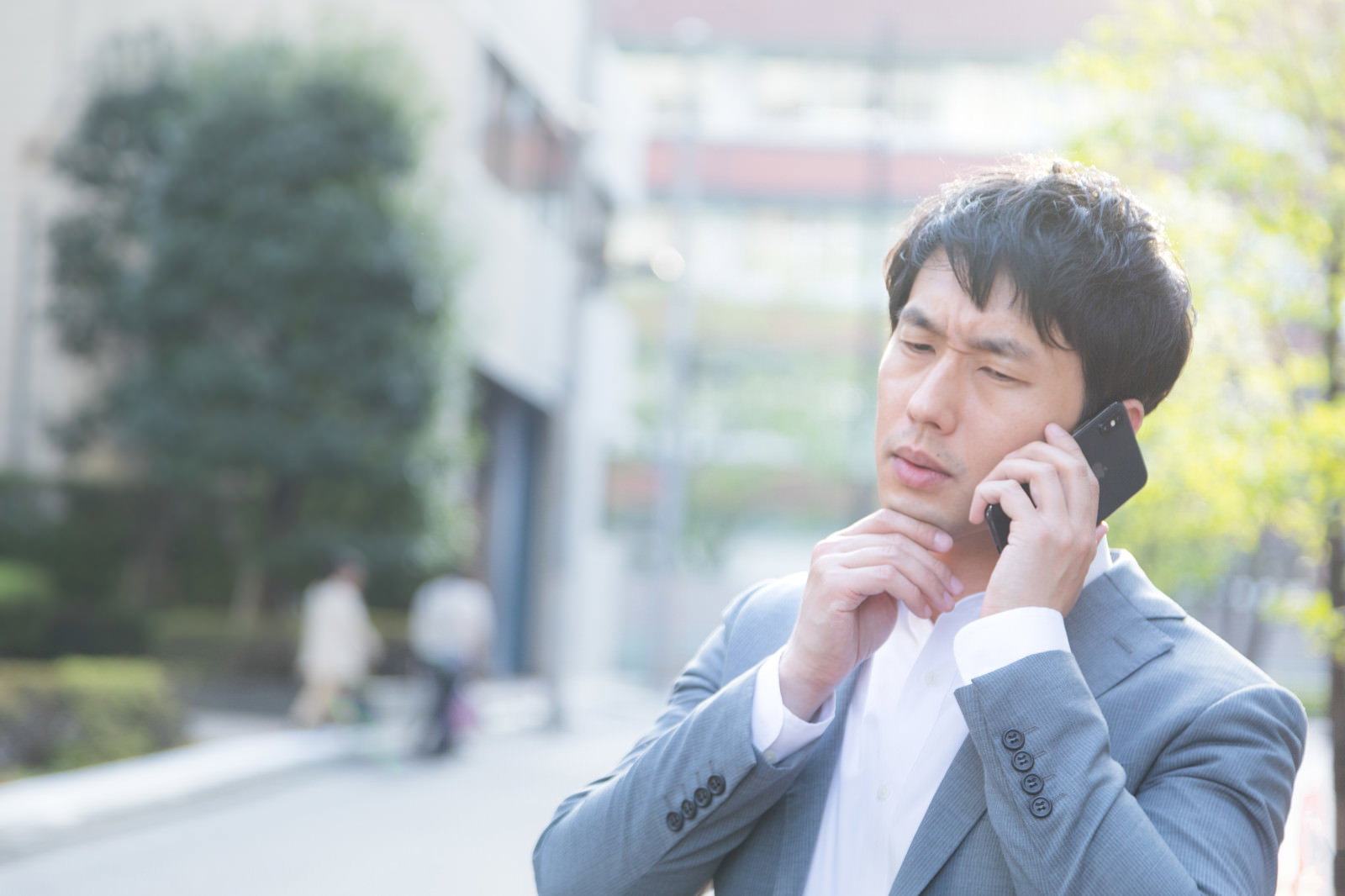 スマートフォンで電話をかけるスーツ姿の会社員男性［モデル：大川竜弥］