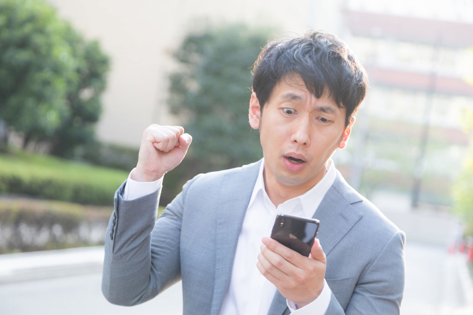 スマートフォンを見て拳を握りしめ怒りの表情を見せる男性［モデル：大川竜弥］