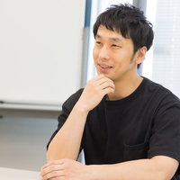 ろくろ回し中のインタビューに答える陶芸職人の男性の写真