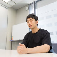 白いテーブルでインタビューに答える黒いシャツの男性の写真