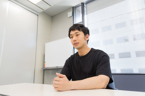 白いテーブルでインタビューに答える黒いシャツの男性