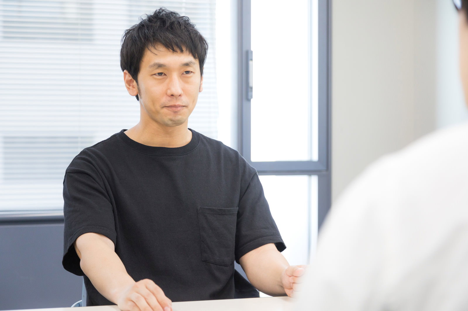 インタビューを受ける緊張した表情の黒いTシャツの男性［モデル：大川竜弥］