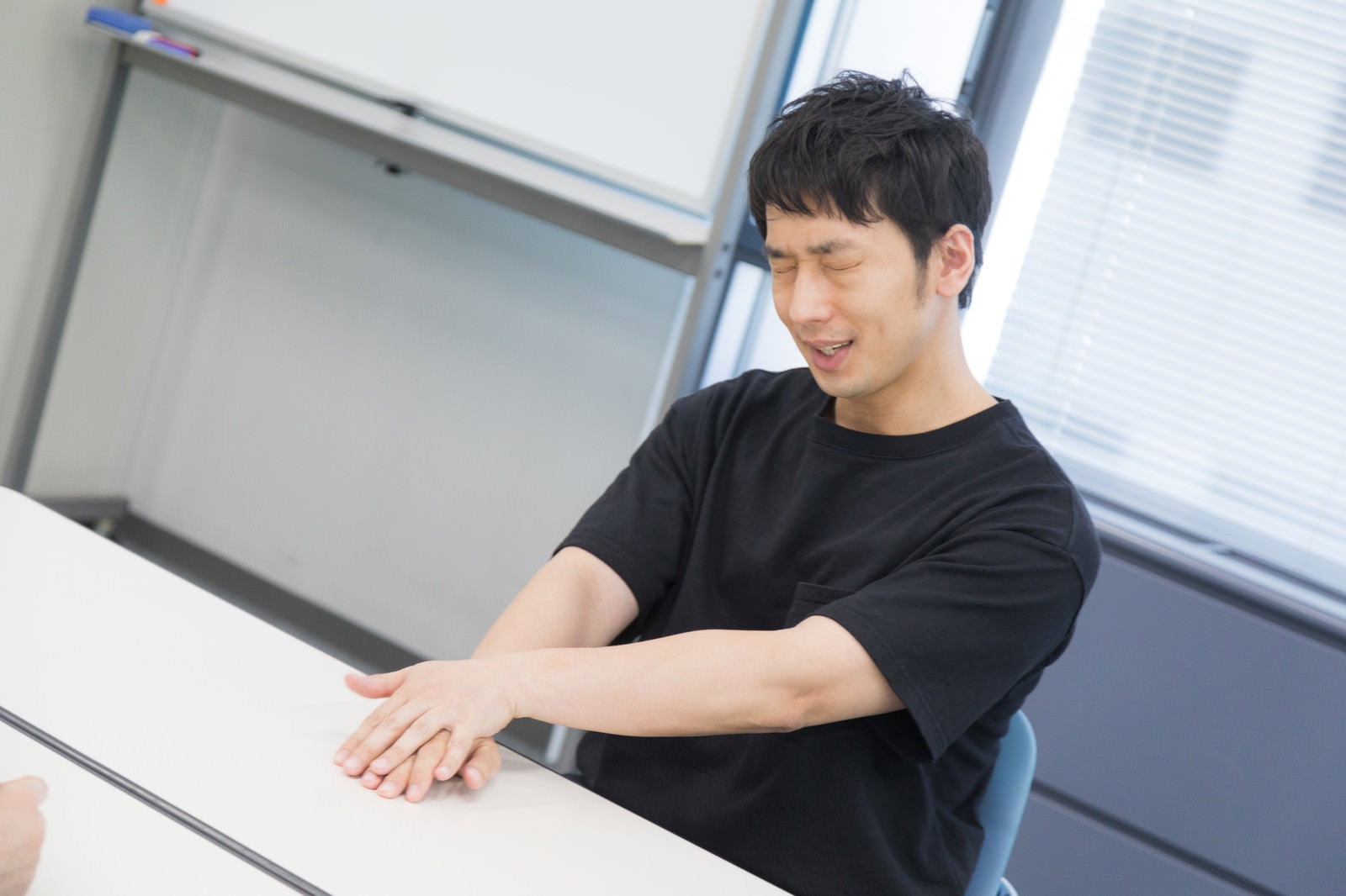 オフィスの会議室で黒いTシャツを着てインタビューを受ける男性［モデル：大川竜弥］
