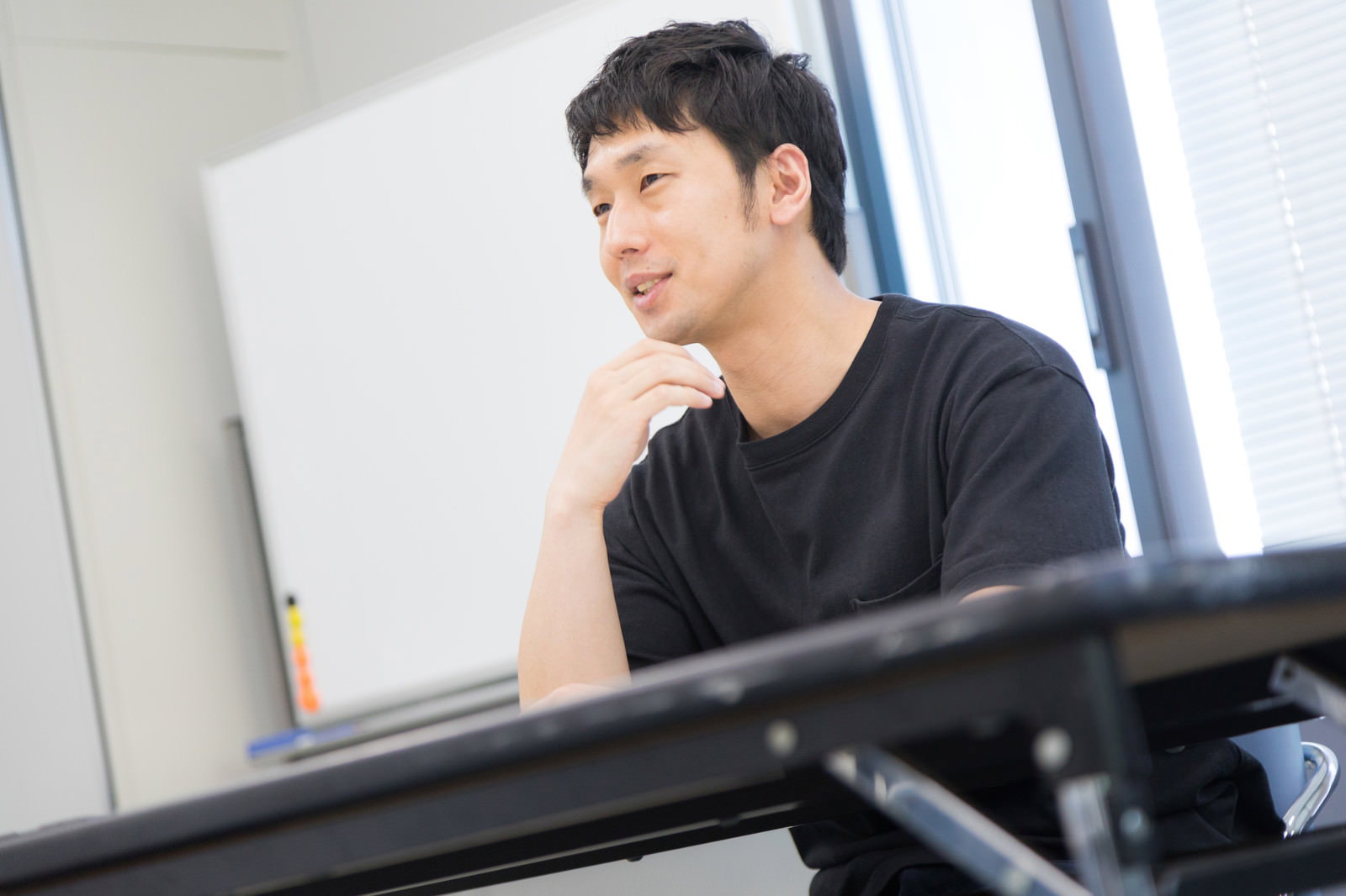 在庫管理のコツを語るECサイト運営者、黒いシャツを着た男性が手を顎に当てて話している［モデル：大川竜弥］