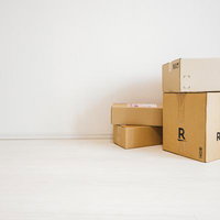 白い部屋の隅に積み重ねられたダンボール箱と配送伝票の写真