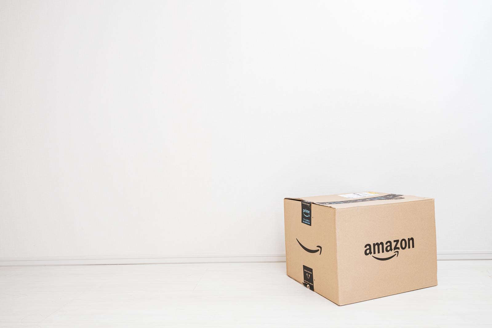 Amazonのロゴが入った茶色い段ボール箱が白い壁の前に置かれている