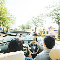 街中をオープンカーで颯爽と駆け抜けるカップルのドライブの写真