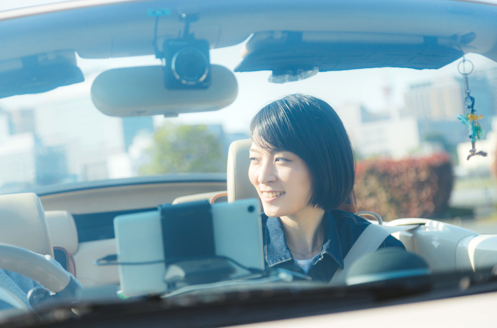 オープンカーの助手席に座り、青空の下で笑顔を見せる女性［モデル：たけべともこ］
