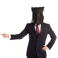 黒い袋をかぶって指をさす黒子スタイルのビジネスマンの写真