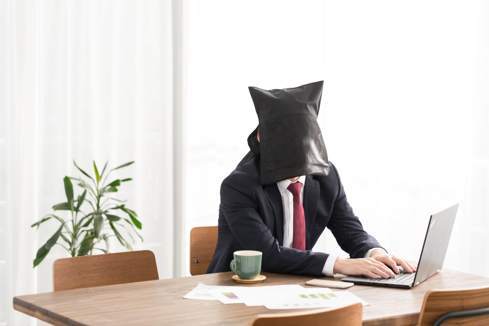 黒い紙袋を頭にかぶりコーヒーをこぼしそうなスーツ男性［モデル：鈴木秀］