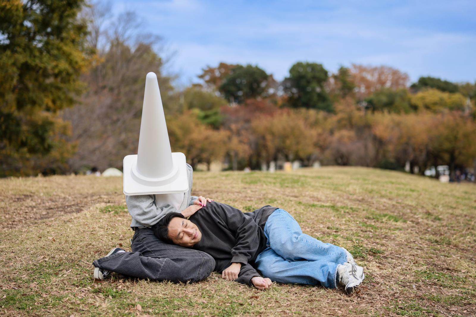 三角コーンを被った女性に膝枕をしてもらう男性［モデル：大川竜弥］