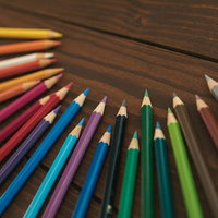 木製テーブルに虹色に並ぶ削った色鉛筆の写真