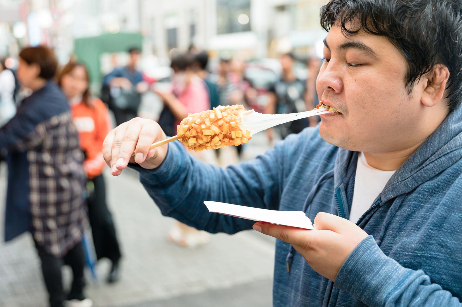 チーズがとろりと伸びるチーズドッグを美味しそうに頬張る男性［モデル：段田隼人］