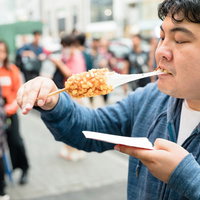 チーズがびろーん伸びるチーズドッグを頬張る男性の写真