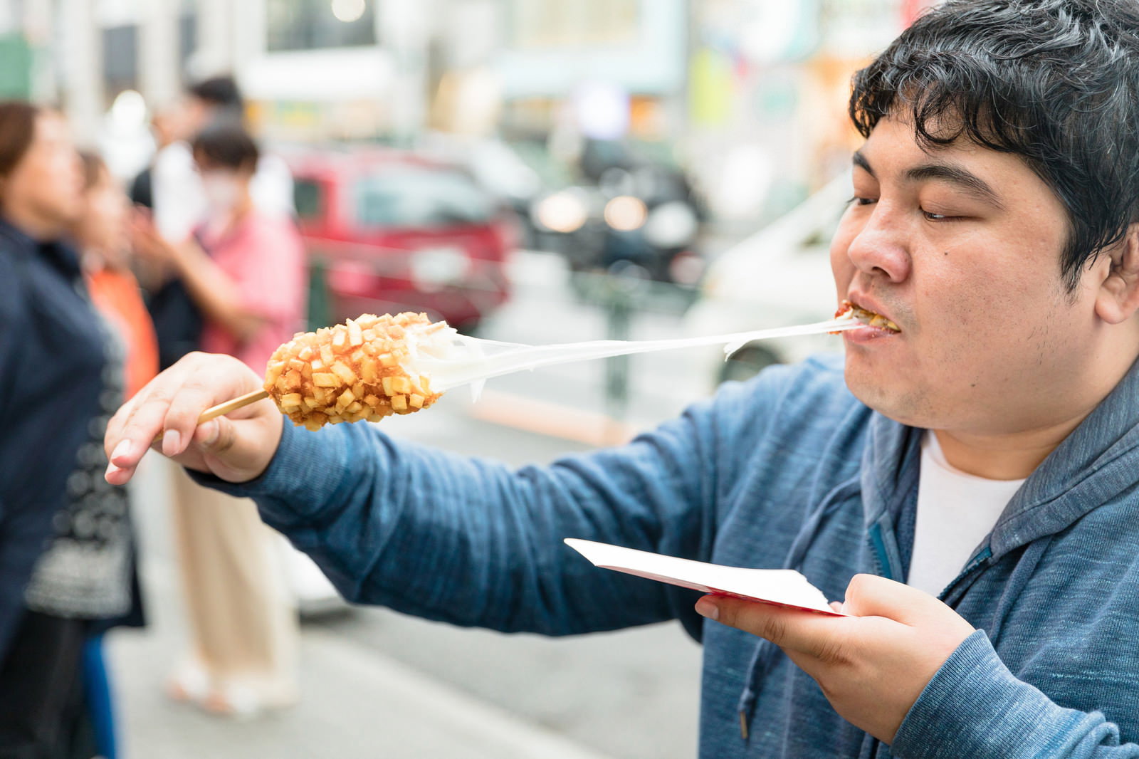 チーズドッグを頬張る男性、伸びるチーズが特徴的な揚げ物［モデル：段田隼人］