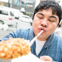 チーズドッグを勢いよく頬張る食いしん坊な男性の写真