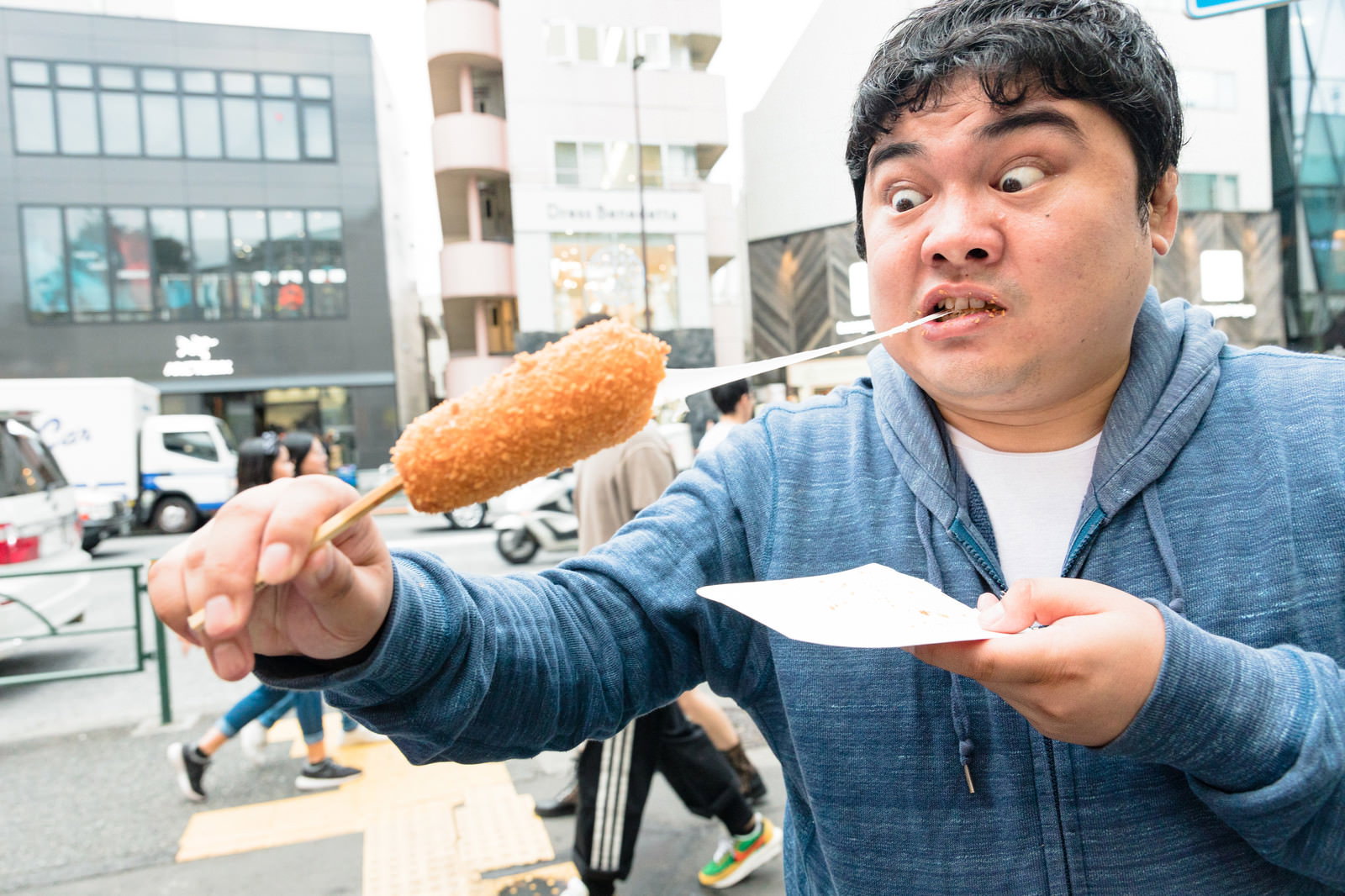 チーズが伸びるチーズドッグを頬張って食べている男性［モデル：段田隼人］