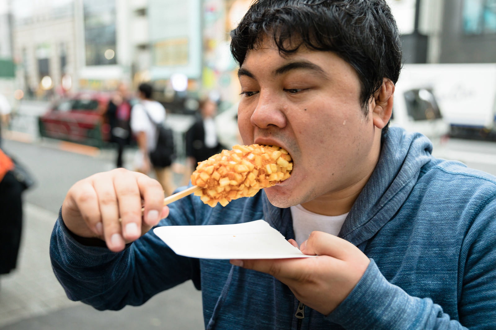 デニムシャツを着た男性がチーズドッグを大きく口を開けて頬張っている［モデル：段田隼人］