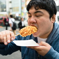 食いしん坊がチーズドッグを大きく頬張る男性の写真