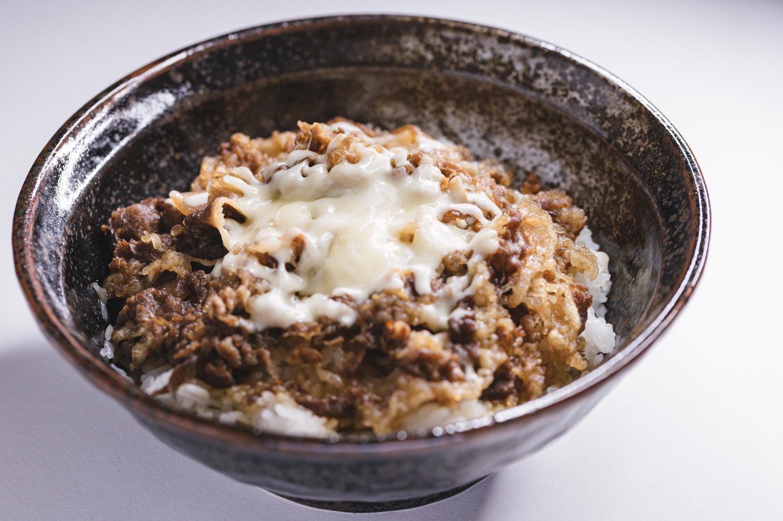 黒い丼に盛られた牛肉そぼろの上に白く溶けたチーズがかかった牛丼