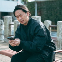 近所の公園のベンチでスマホゲームに夢中になるアラフォー男性の写真