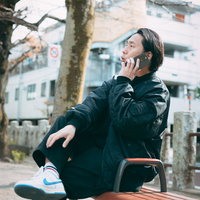 公園のベンチで昼間からスマホで指示を送る男性の写真