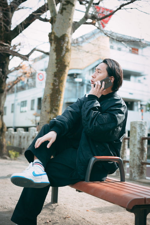 公園のベンチで昼間からスマホで指示を送る男性