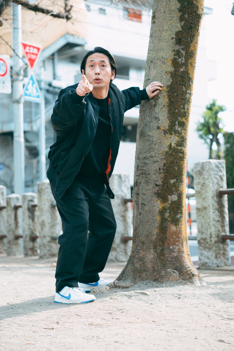 公園の樹の幹に手をついてだるまさんがころんだで人を指す男性［モデル：大川竜弥］