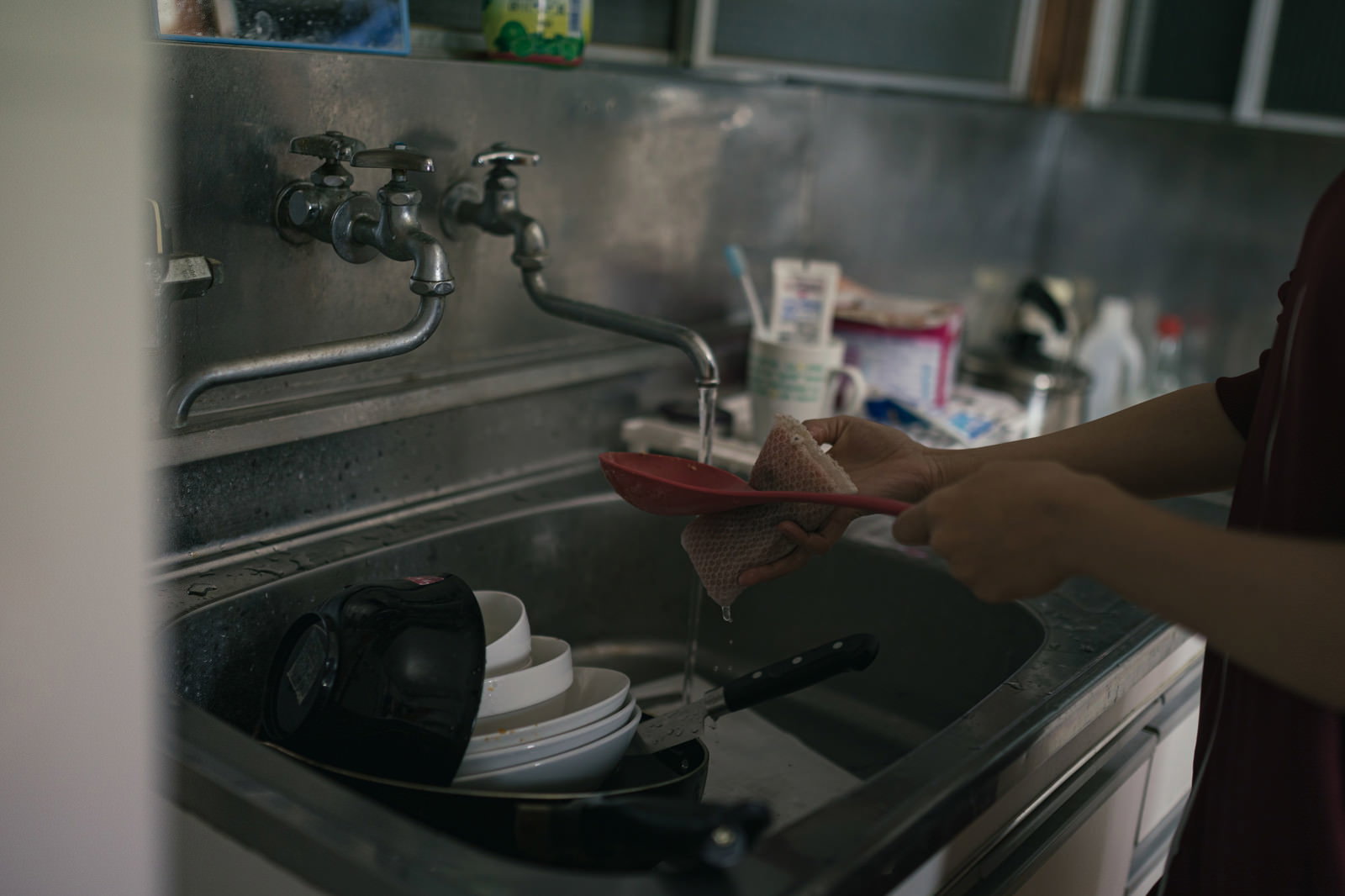 食器や調理器具が溜まったキッチンのシンクでスポンジを使って洗い物をしている様子