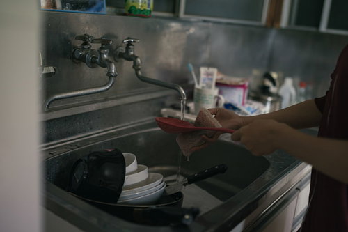 洗い物が溜まったキッチンのシンクをスポンジで洗う様子