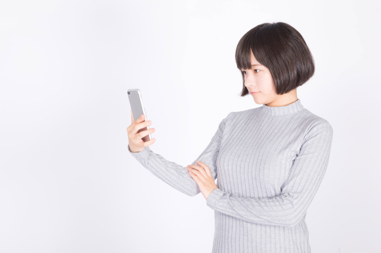 グレーのニットを着た女性がスマートフォンを手に持ち画面を確認している［モデル：千歳］