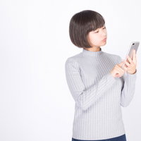グレーニットを着てスマホで検索中の女性のスマートフォン操作の写真