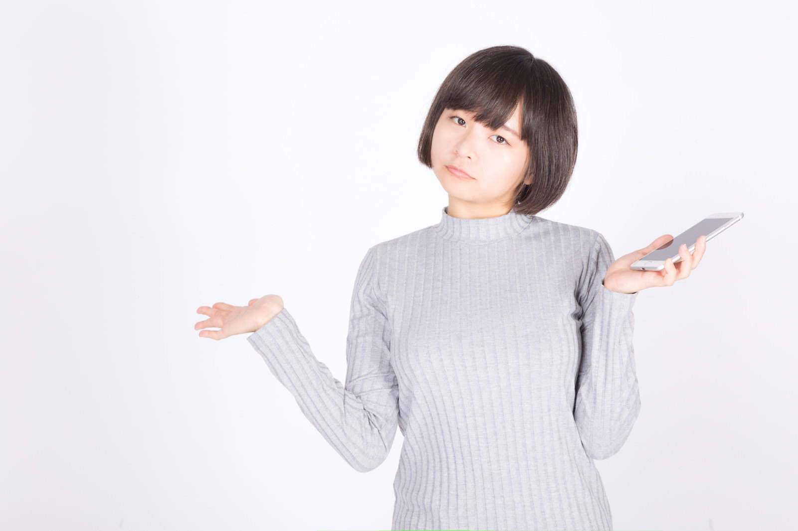 グレーセーターを着た女性がスマートフォンを持ち、両手を広げて困った表情で上を向いている［モデル：千歳］