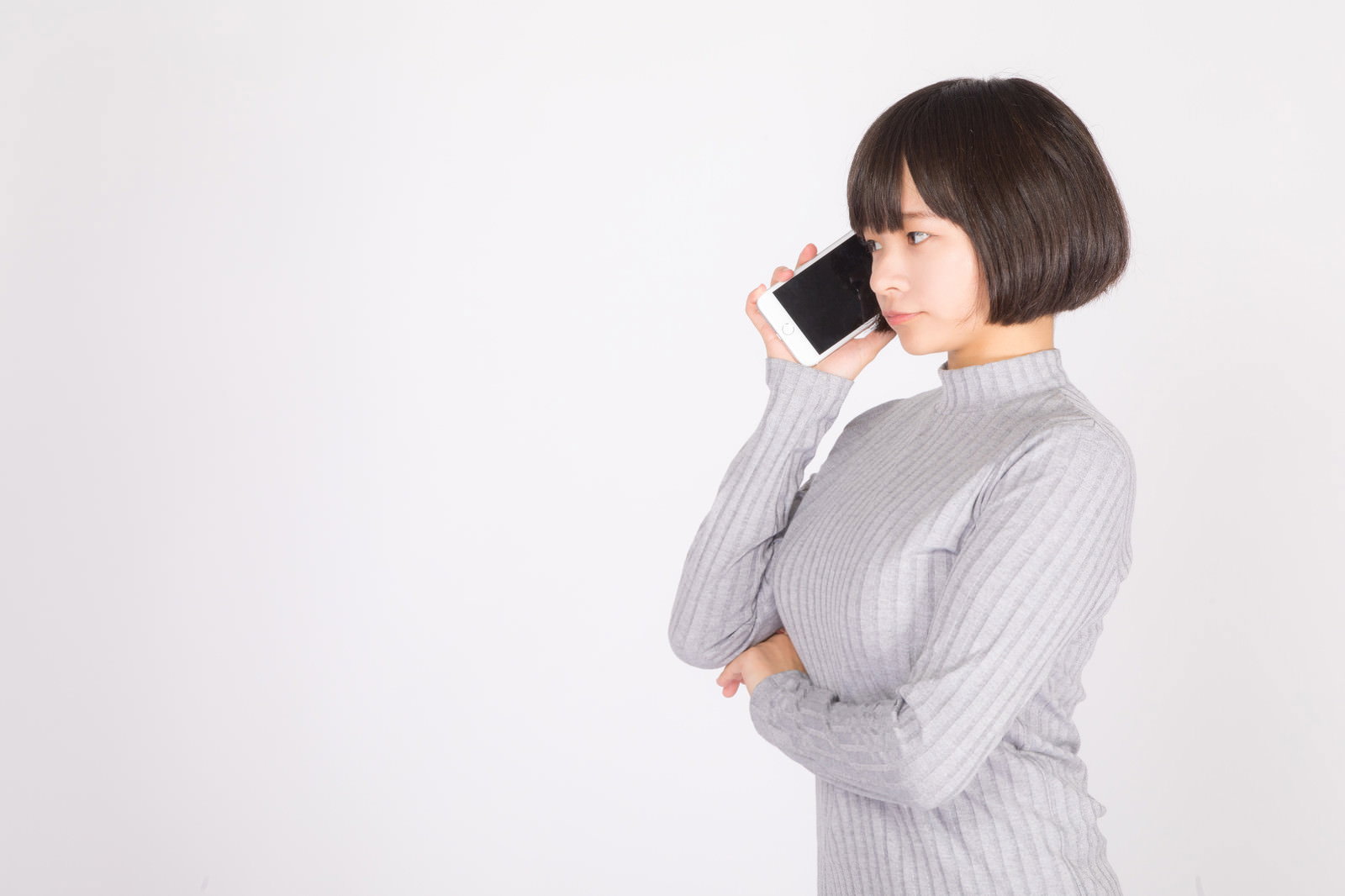 グレーのニットを着た女性がスマートフォンで通話している［モデル：千歳］