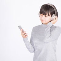 ワイヤレスヘッドホンでスマホの音楽を楽しむ女性の写真