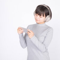 ワイヤレスヘッドホンでスマホで映画を見る女性の写真