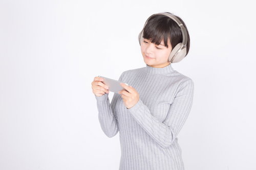 ワイヤレスヘッドホンでスマホで映画を見る女性