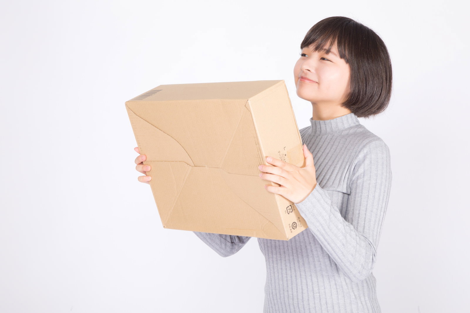 茶色のダンボール箱を両手で抱えて嬉しそうに笑う女性［モデル：千歳］