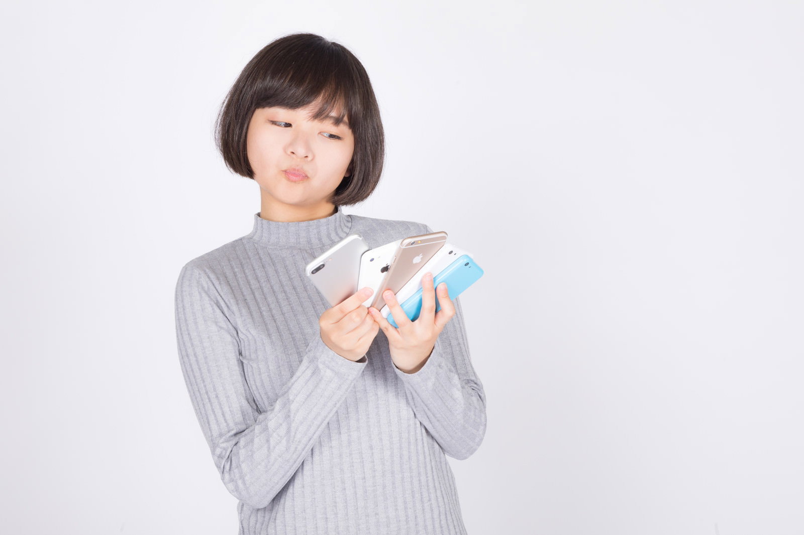 グレーのニットを着た女性が複数台のスマートフォンを手に持っている［モデル：千歳］
