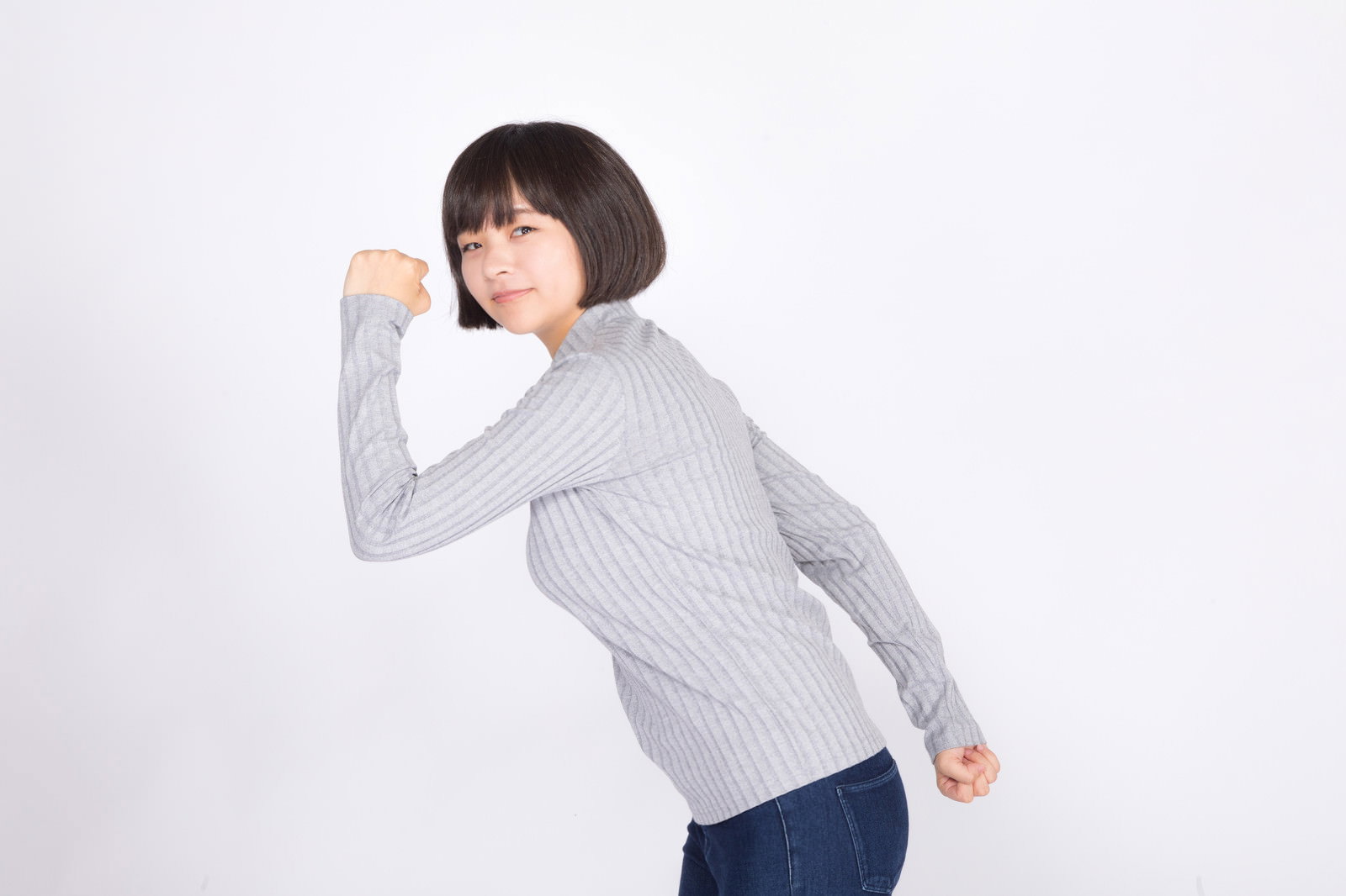 グレーのトップスを着た女性が白背景でダッシュしている［モデル：千歳］